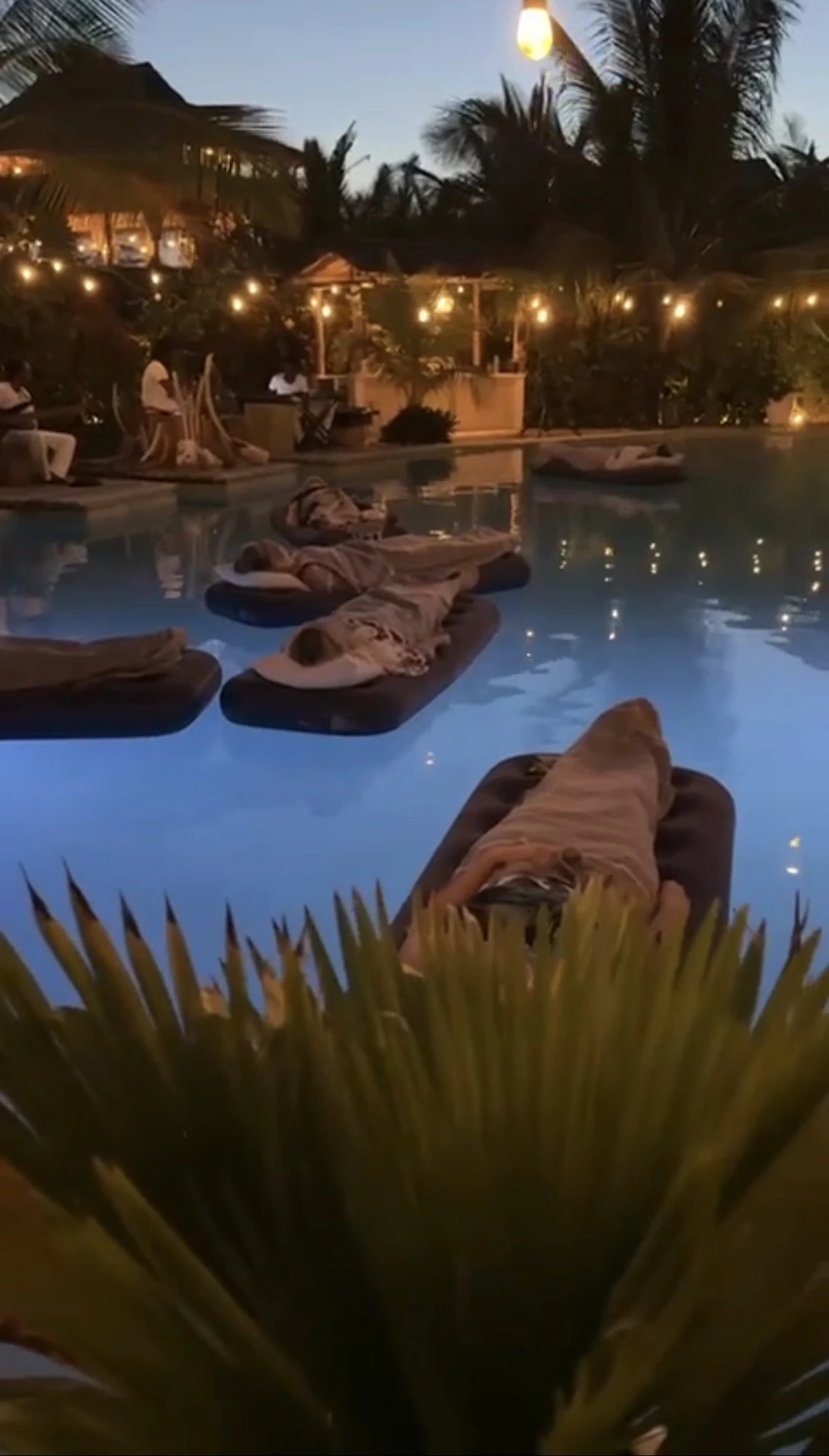 Guests floating on the pool at night among candlelit lanterns — an evening of unwinding